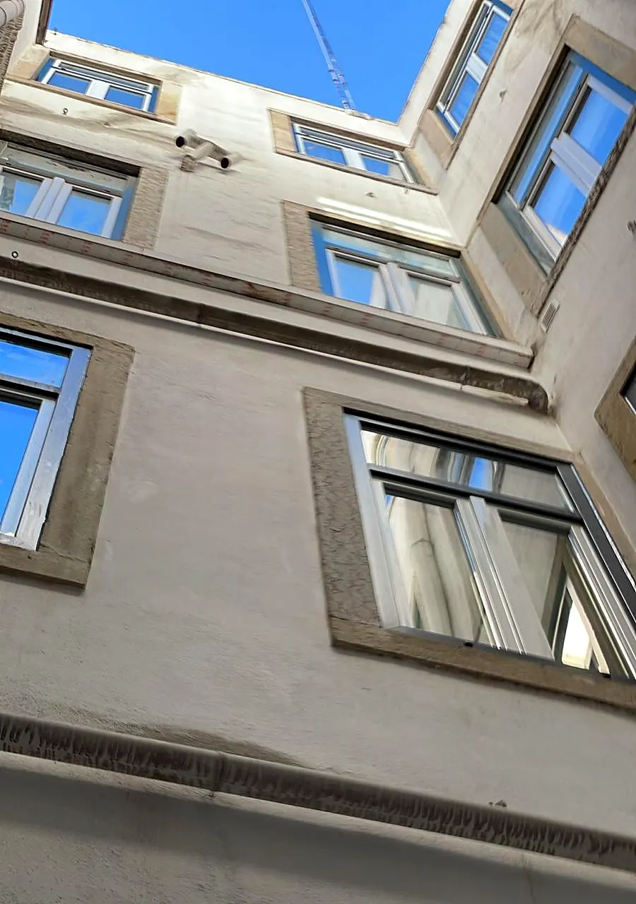 Saguão de edifício antigo visto de baixo, com janelas e tubagens a reabilitar